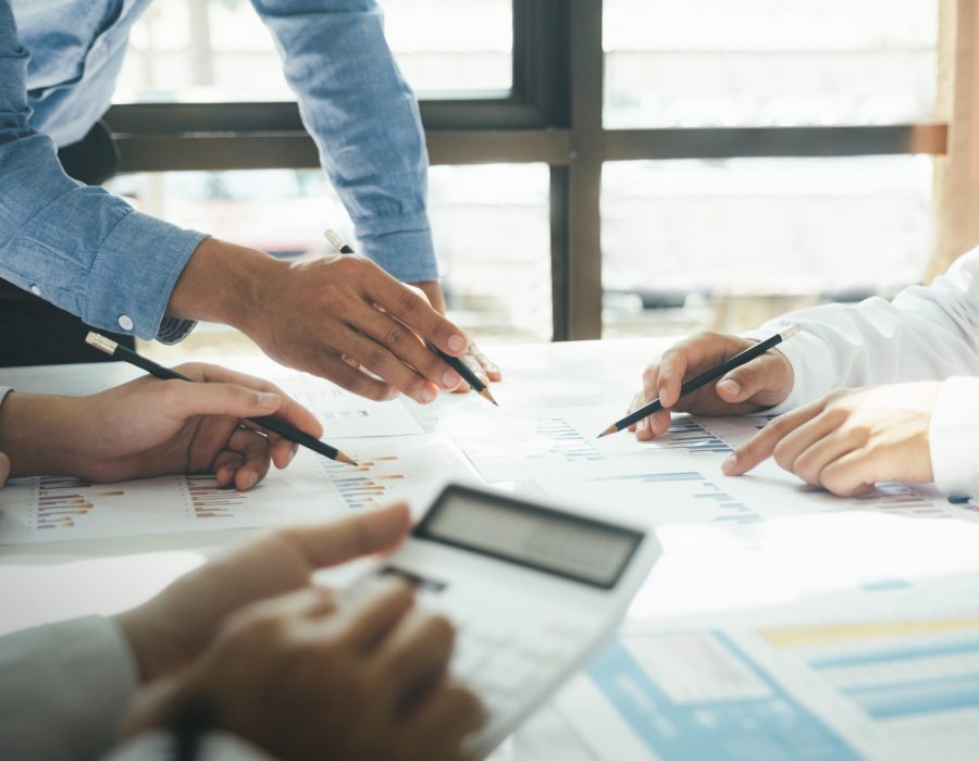 Close-up of businessmen working together at workplace, discussing  about strategies, plans, analytic progress, and financial stats, and pointing at graph documents on desk holding pencils and calculator. Business and Teamwork concept.